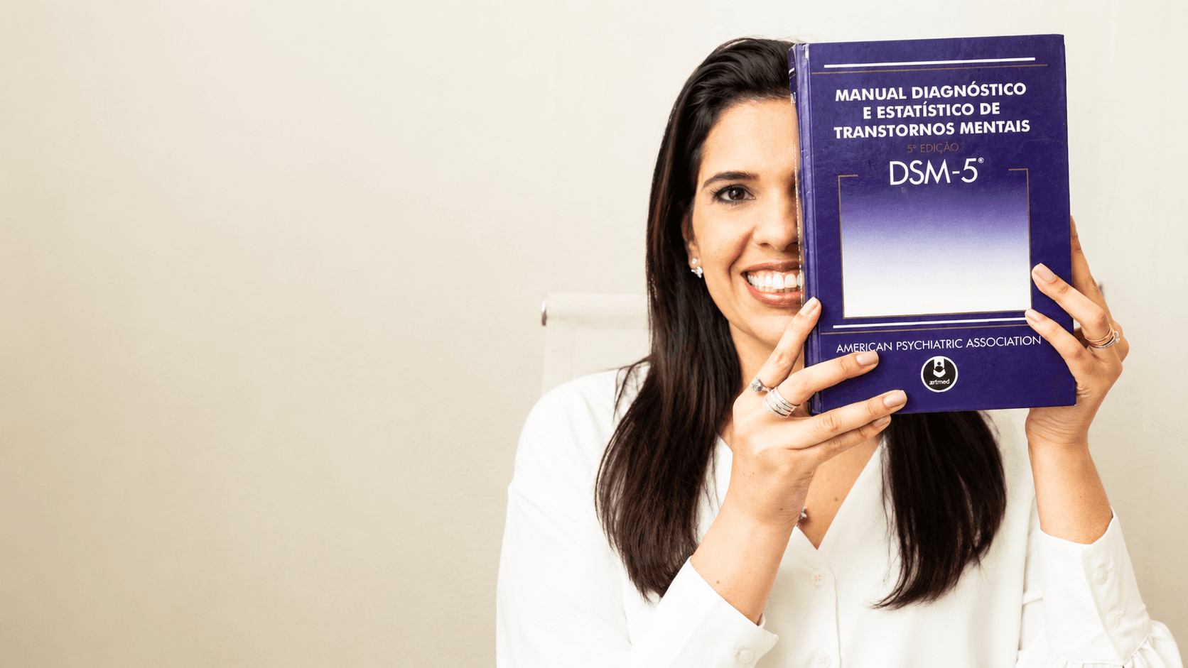 Imagem da Dra. Aline Rangel, médica psiquiatra, psicoterapeuta e sexóloga, segurando o Manual Diagnóstico e Estatístico de Transtornos Mentais, DSM-5. Foto utilizada como imagem destacada de artigo sobre avaliação psiquiátrica, diagnóstico e critérios clínicos.