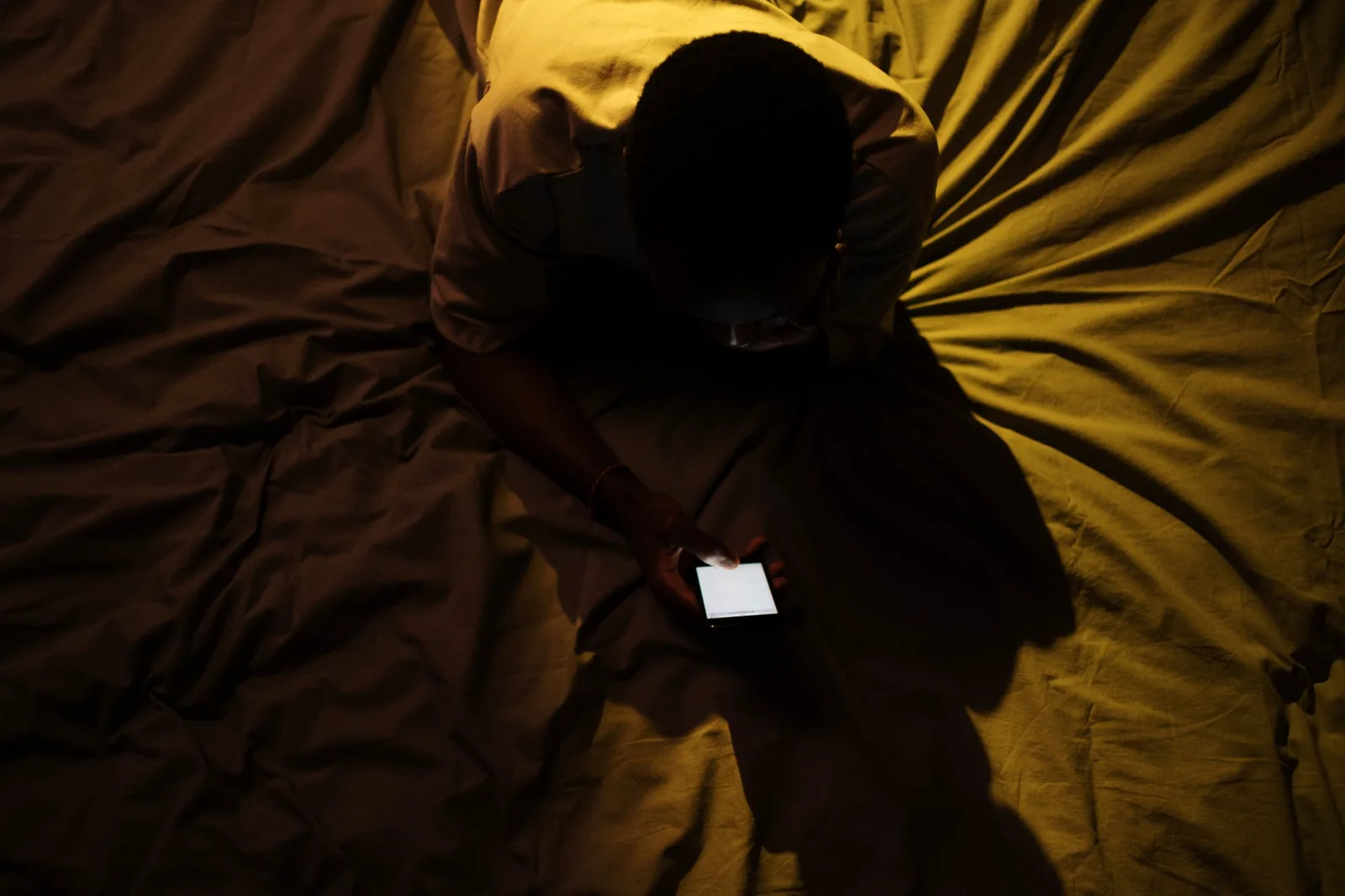 Homem sentado na cama usando o celular à noite, em artigo sobre uso problemático de pornografia.