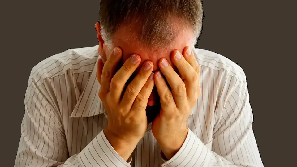 Homem com as mãos sobre o rosto em gesto de sofrimento emocional.