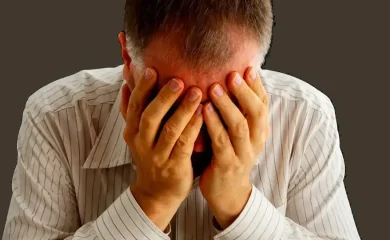 Homem com as mãos sobre o rosto em gesto de sofrimento emocional.
