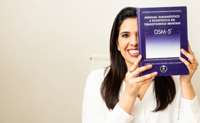 Imagem da Dra. Aline Rangel, médica psiquiatra, psicoterapeuta e sexóloga, segurando o Manual Diagnóstico e Estatístico de Transtornos Mentais, DSM-5. Foto utilizada como imagem destacada de artigo sobre avaliação psiquiátrica, diagnóstico e critérios clínicos.