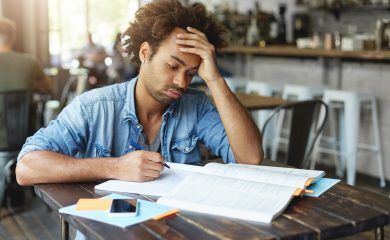 Tired Afro American college student with curly hairstyle blowing out his cheeks looking bored or fed up, losing patience while failing to solve complicated mathematical problem, doing home assignment